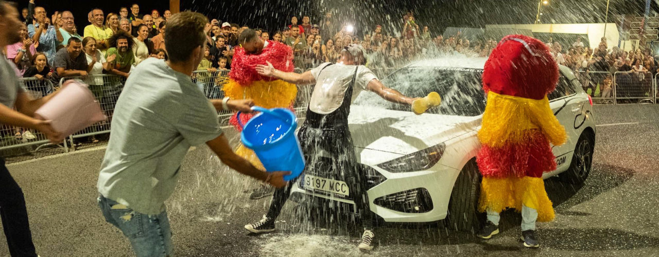 Clown Show and Improvisation Theater - Unforgettable Street Mime Spectacle in Car Wash. Agro le clown recevant un seau d'eau d'un spectateur à côté d'une voiture entourée de public. Luca Della Gatta