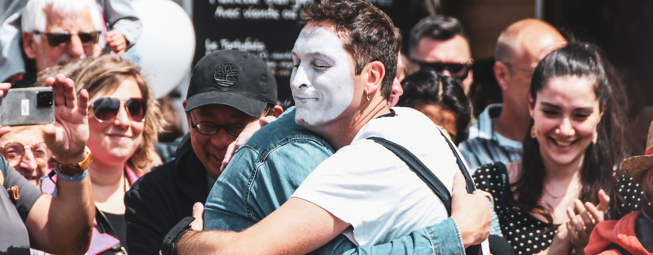 Street Performers Come Alive ! Agro the Clown’s Unique Solo Performance in Improlocura. Agro hugging a spectator with a crowd in the background. Luca Della Gatta. Luca Della Gatta